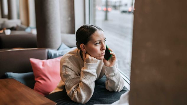 Kvinde sidder og kigger ud af billedet og taler i telefon